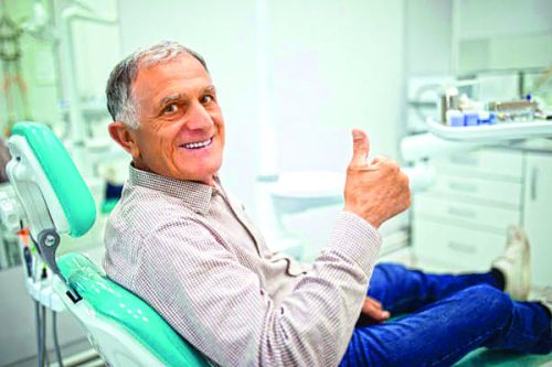 Old senior man sitting in a dental chair thumb up